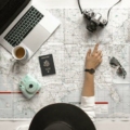 mulher analizando mapa do mundo, em cima do mapa tem um óculos, uma câmera, passaporte, café e um notebook