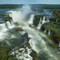 Vista das Cataratas do Iguaçu com passarela de turistas e arco-íris ao fundo