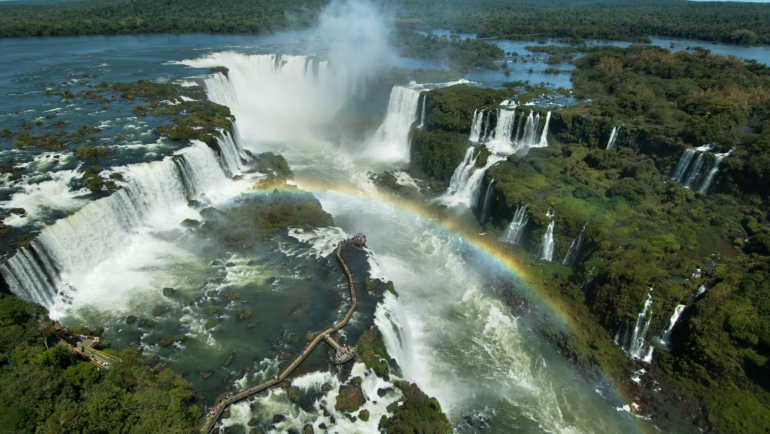 Vista das Cataratas do Iguaçu com passarela de turistas e arco-íris ao fundo